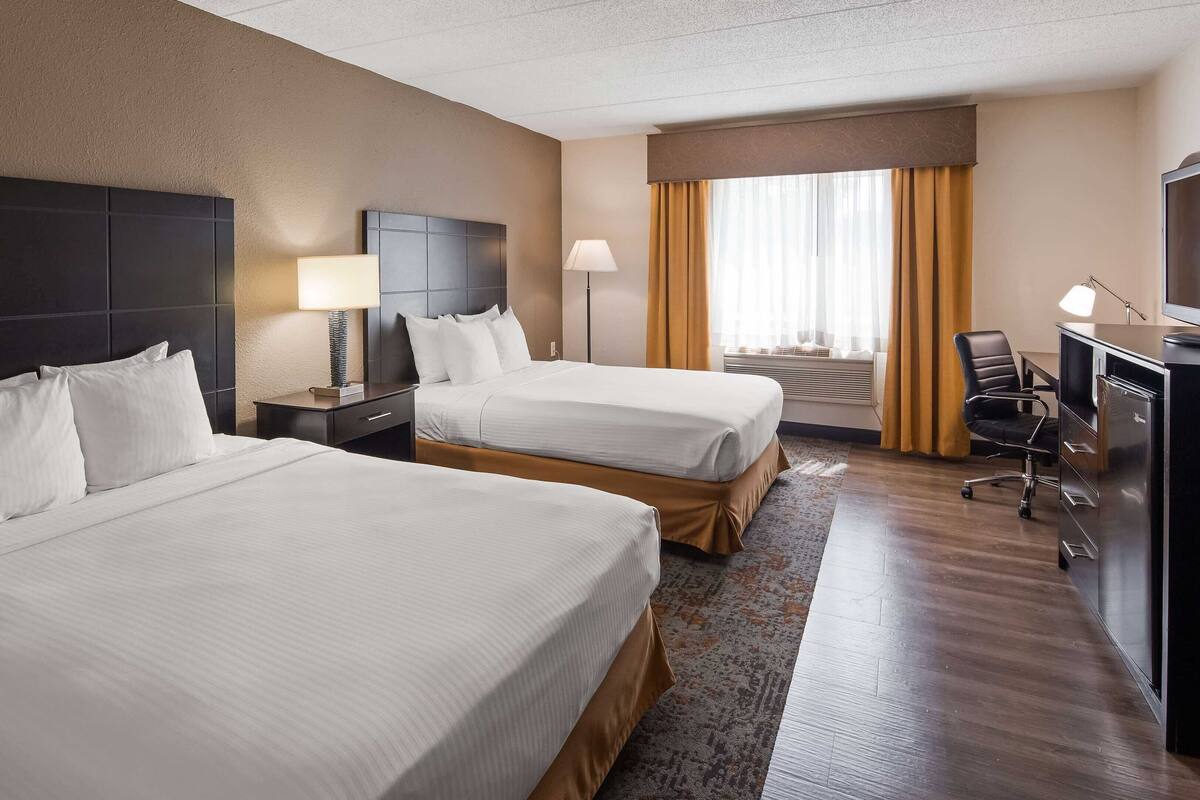 A hotel room with two beds, a desk, a chair, a TV, and a window with curtains.