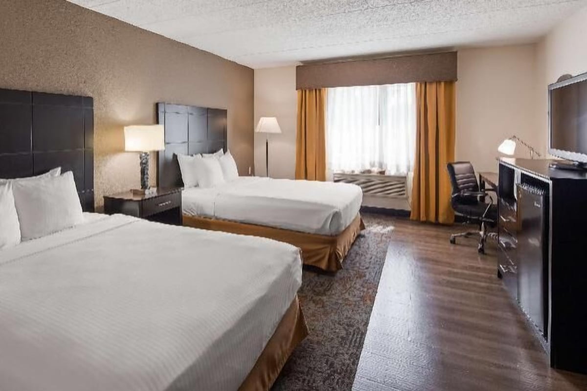 A hotel room with two beds, a desk, a chair, a TV, and a window with curtains.