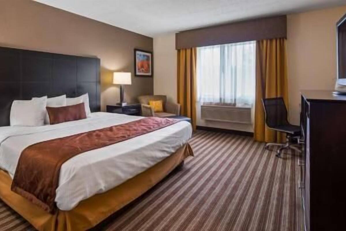 A hotel room with a large bed, a desk, a chair, a lamp, and a window with curtains.