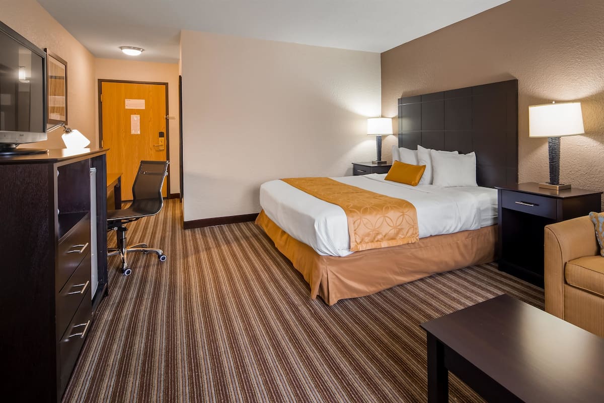 A hotel room with a large bed, a desk, a chair, a sofa, and a TV.