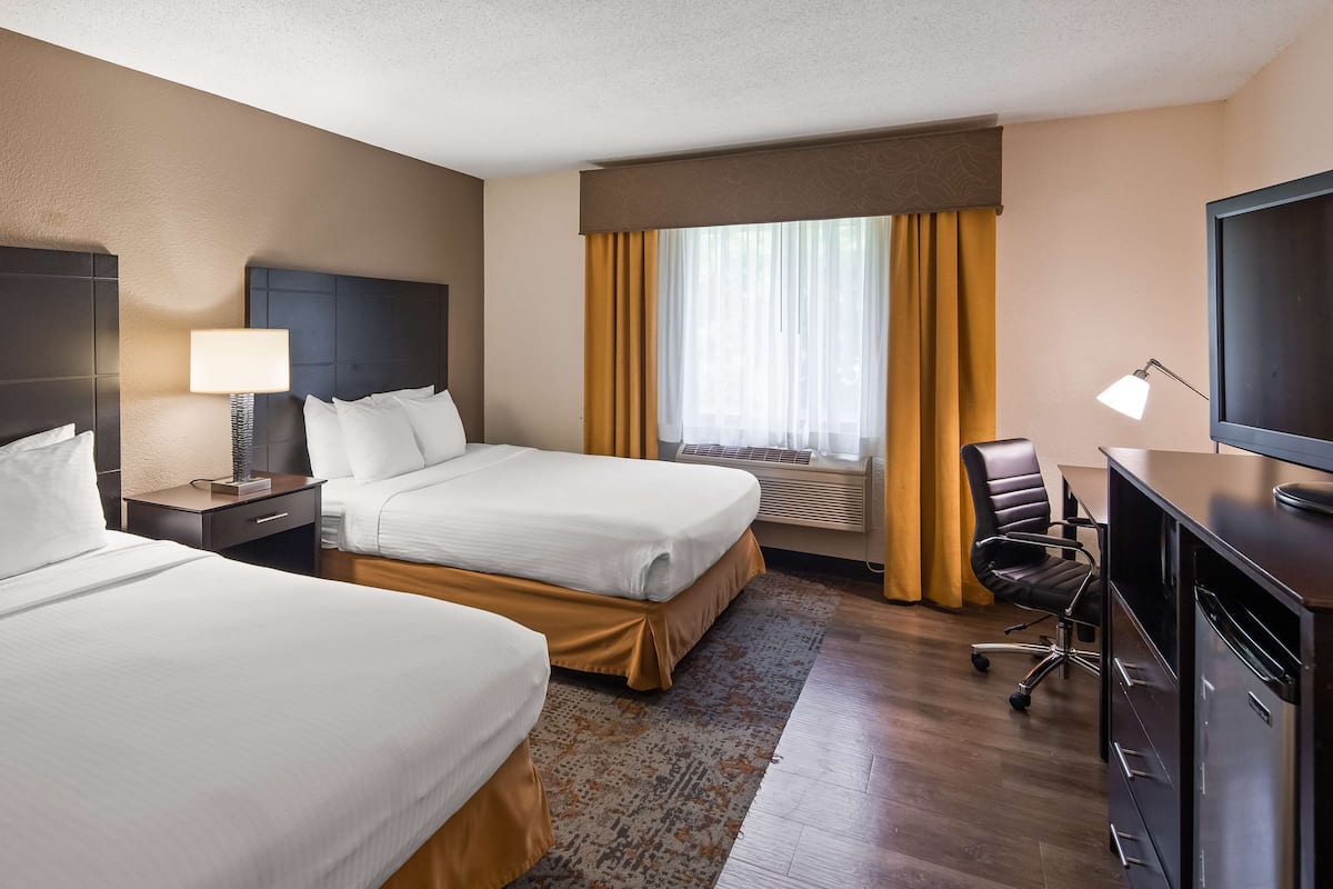 A hotel room with two beds, a desk, a chair, a TV, and a window with curtains.