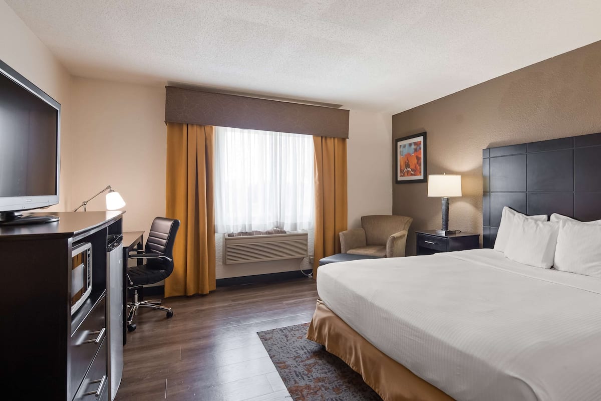 A hotel room with a large bed, a desk with a computer, a chair, a TV, and a window with curtains.