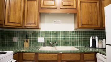 A kitchen with wooden cabinets, a green tiled backsplash, a sink, and a coffee maker.