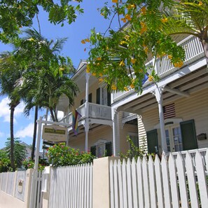 A two-story house with a balcony, a white picket fence, and a flag.