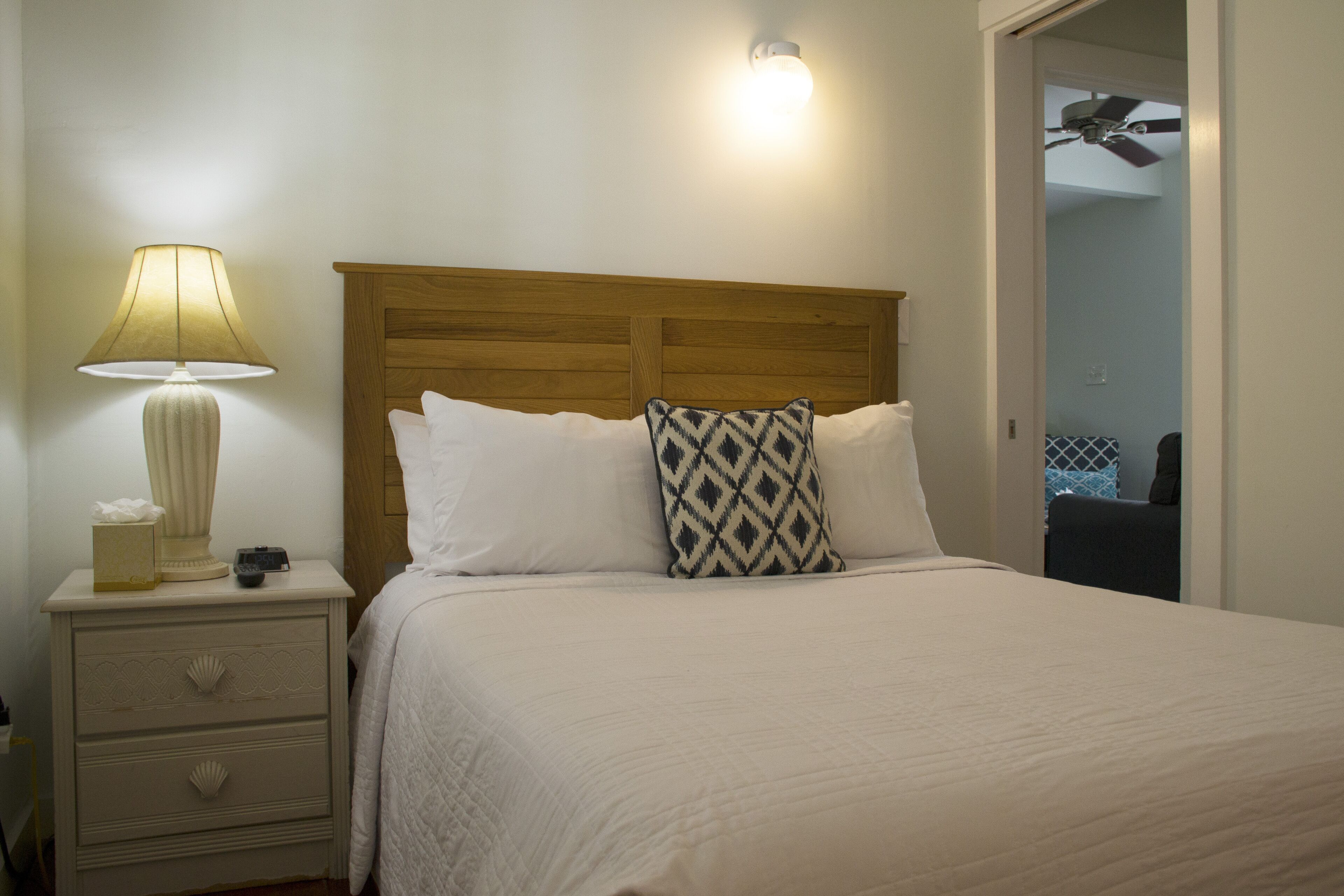 A neatly made bed with a wooden headboard, a bedside lamp, and a nightstand with drawers.
