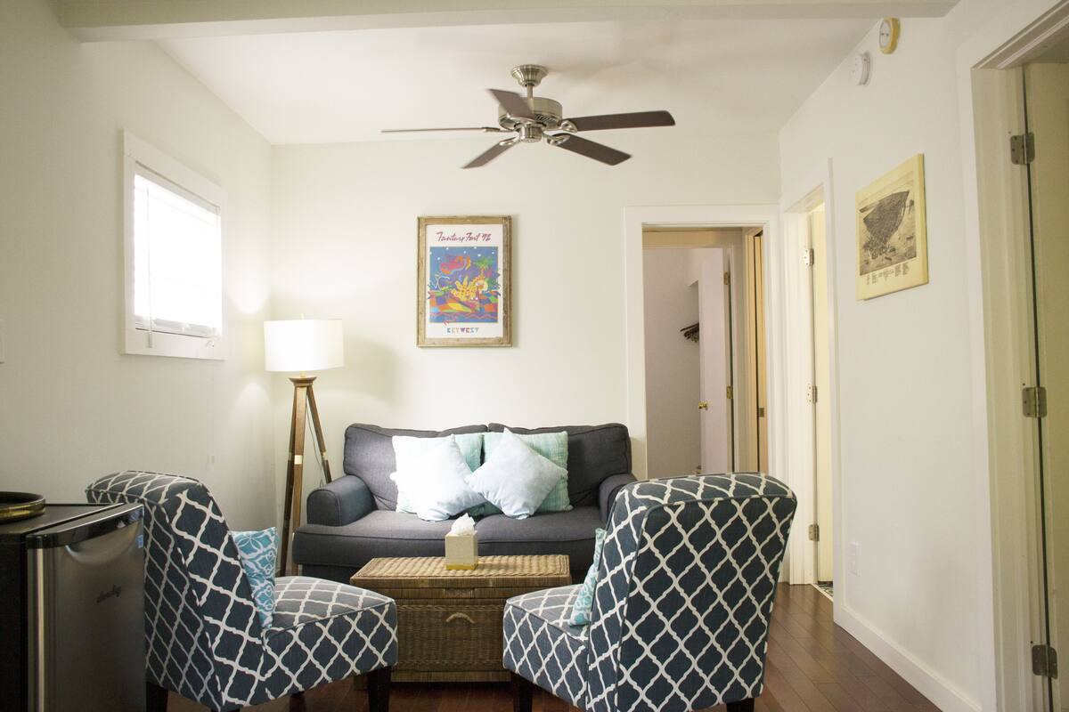 A living room with a sofa, two patterned armchairs, a coffee table, a floor lamp, and a ceiling fan.