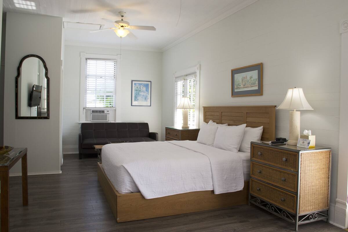 A bedroom with a wooden bed, a nightstand, a dresser, a ceiling fan, and a window with blinds.