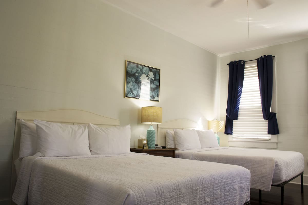 A hotel room with two single beds, a nightstand with a lamp, a framed picture on the wall, and a window with curtains.