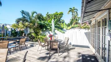 A patio with a round table and chairs, surrounded by a wooden deck and a white fence.
