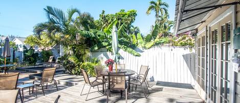 A patio with a round table and chairs, surrounded by a wooden deck and a white fence.