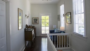 A hallway with a white door, a wooden bench, a blue sofa, and a staircase with a white railing. - Duval House (Key West)