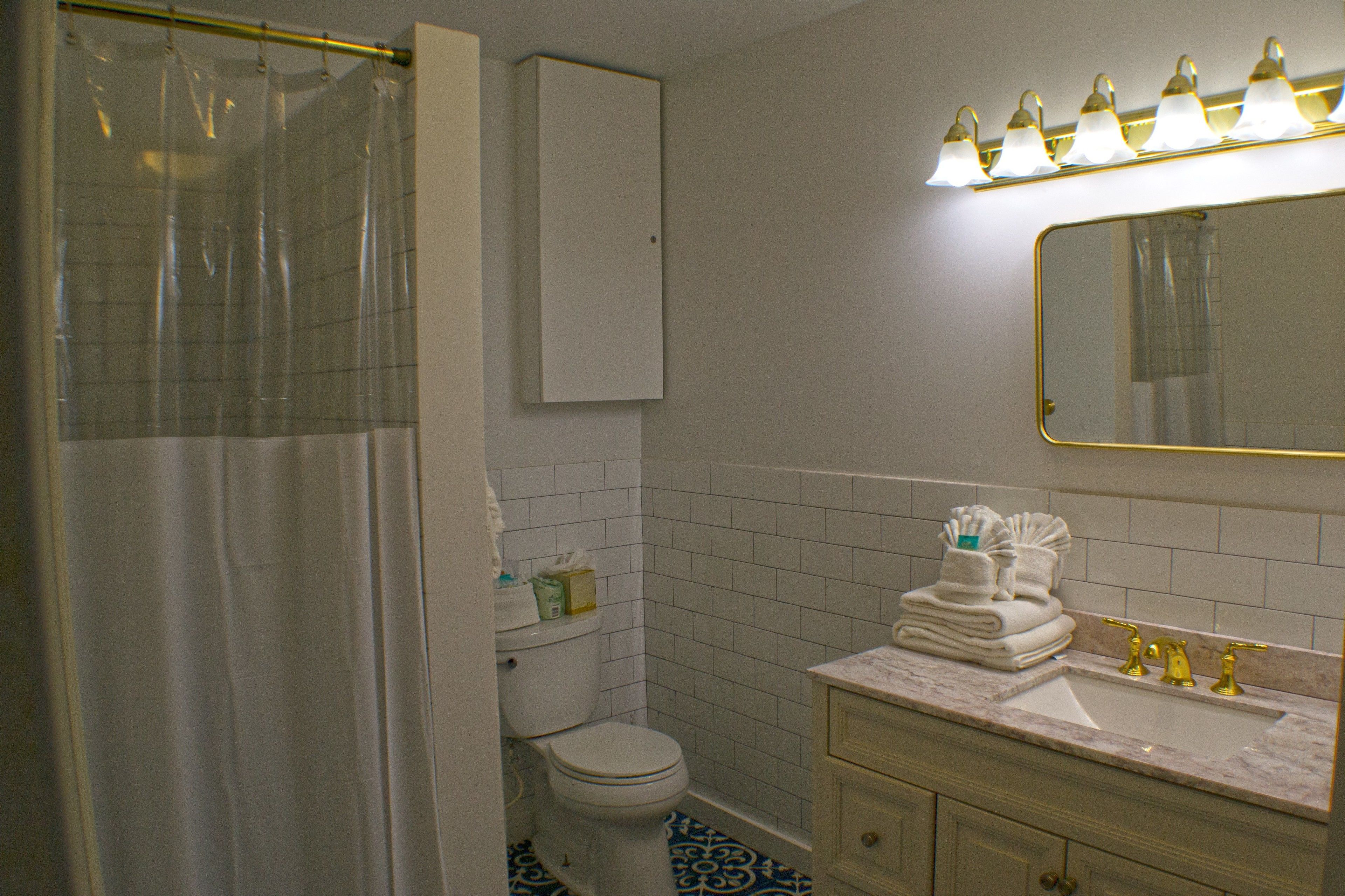 Une salle de bain avec un rideau de douche, des toilettes, un lavabo avec des robinets dorés et un miroir surmonté de lumières.