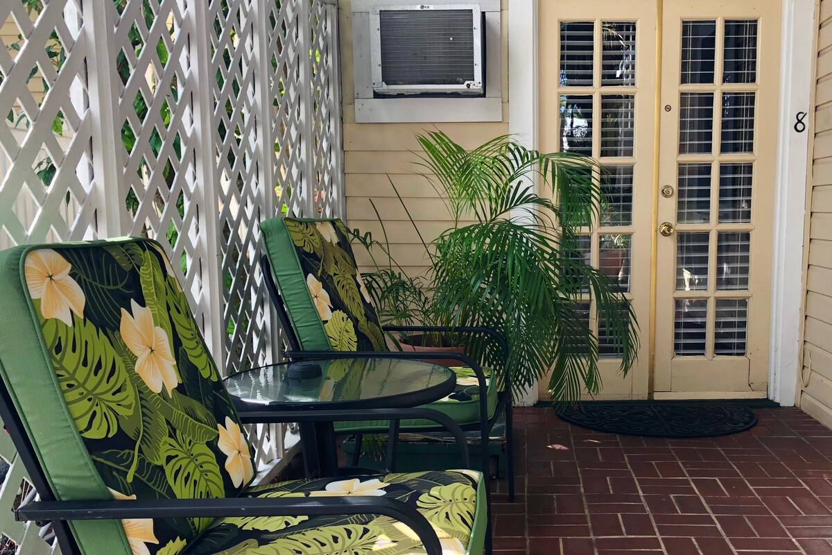 A patio area with two green chairs, a table, and a potted plant.