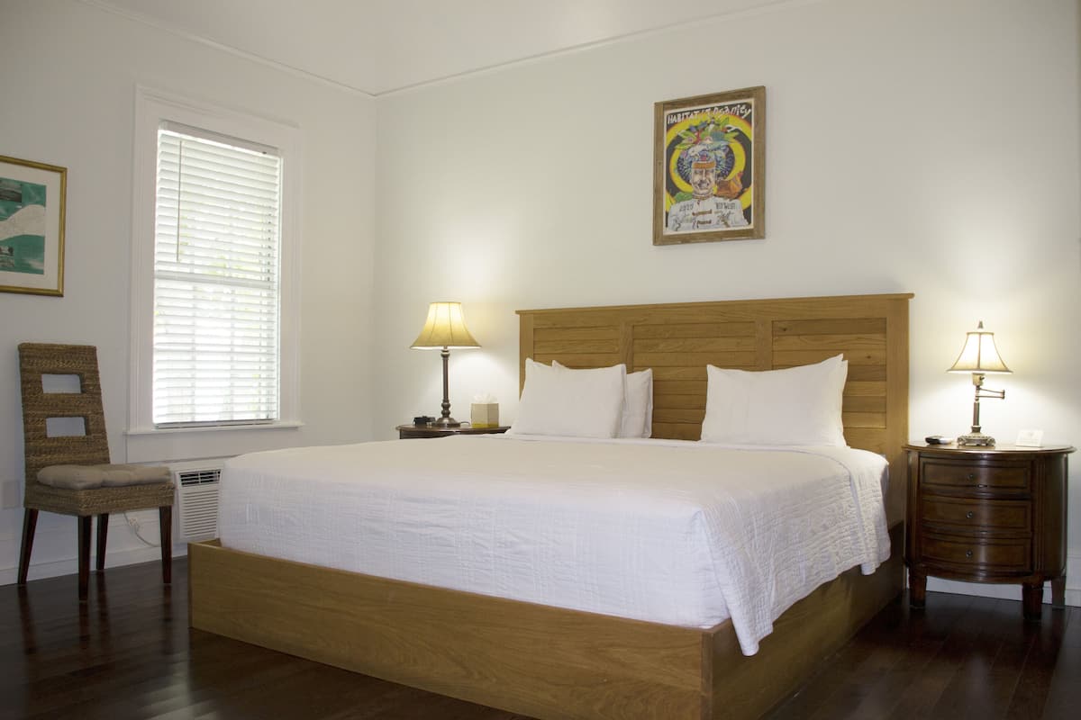 A neatly made bed in a room with a wooden headboard, a chair, and a bedside table with a lamp.