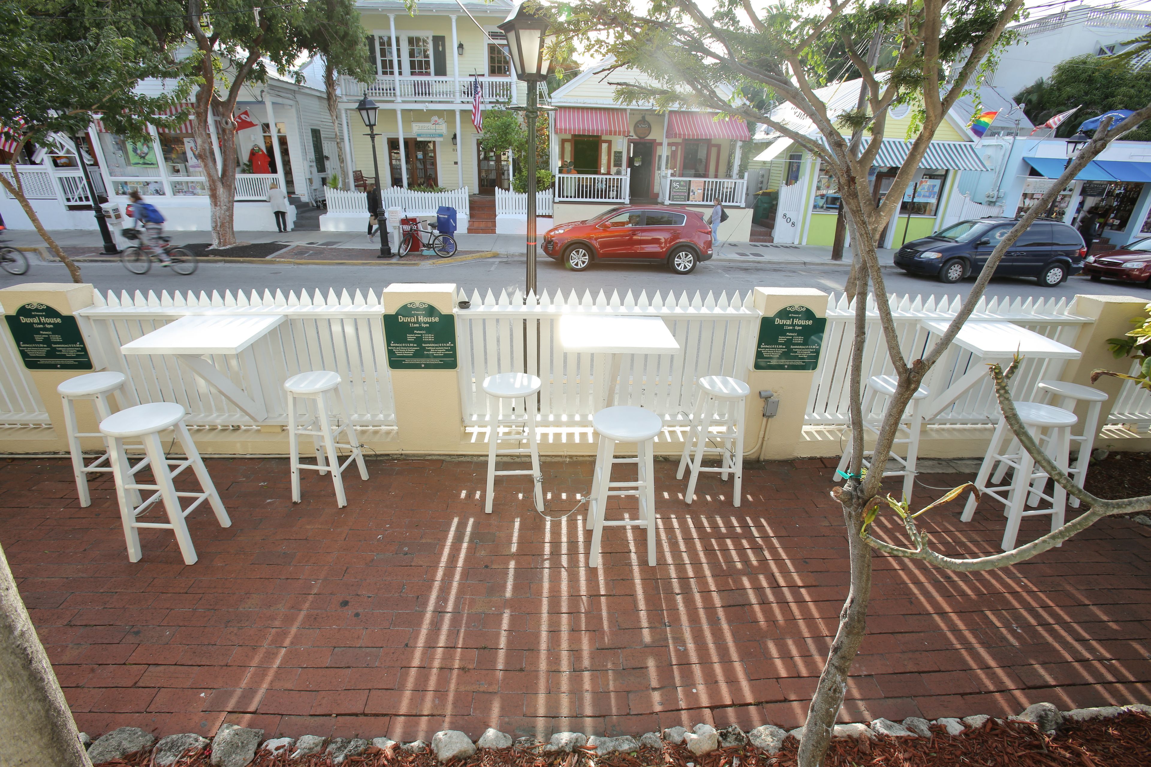 A patio area with white tables and chairs, a brick floor, and a white picket fence.