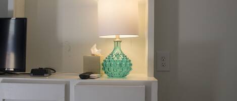 A room with a television on a stand, a green vase with a lamp, and a tissue box.