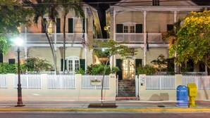 A two-story building with a white picket fence, a mailbox, and a small tree in front. - Duval House (Key West)