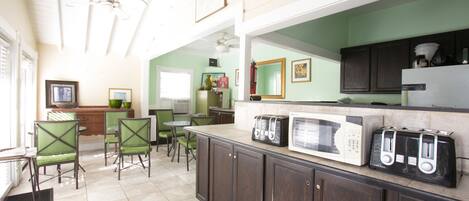 A kitchen with dark wooden cabinets, a microwave, and a toaster. There are two chairs and a table in the dining area.