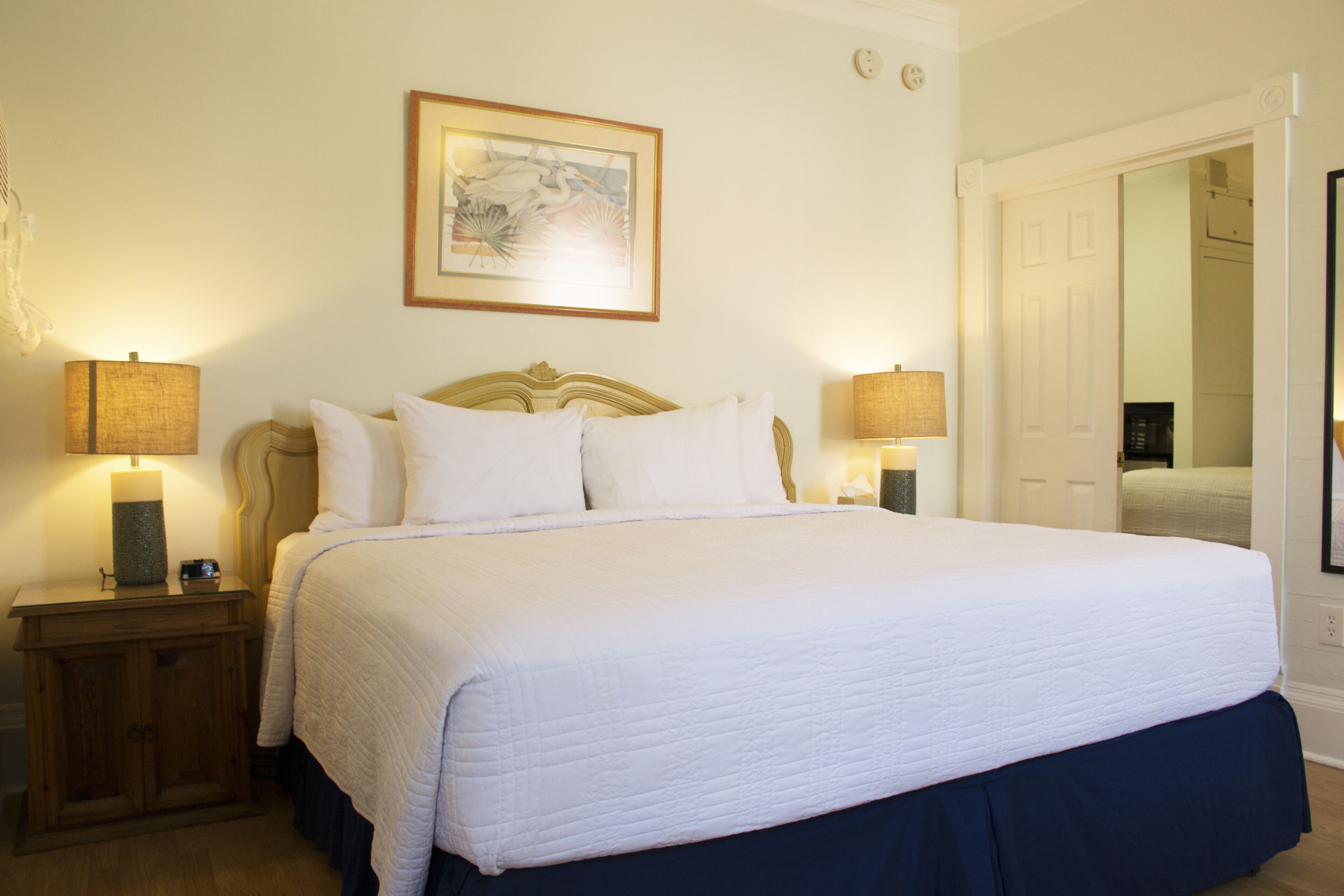 A neatly made bed with white linens, two bedside tables with lamps, and a framed picture on the wall.