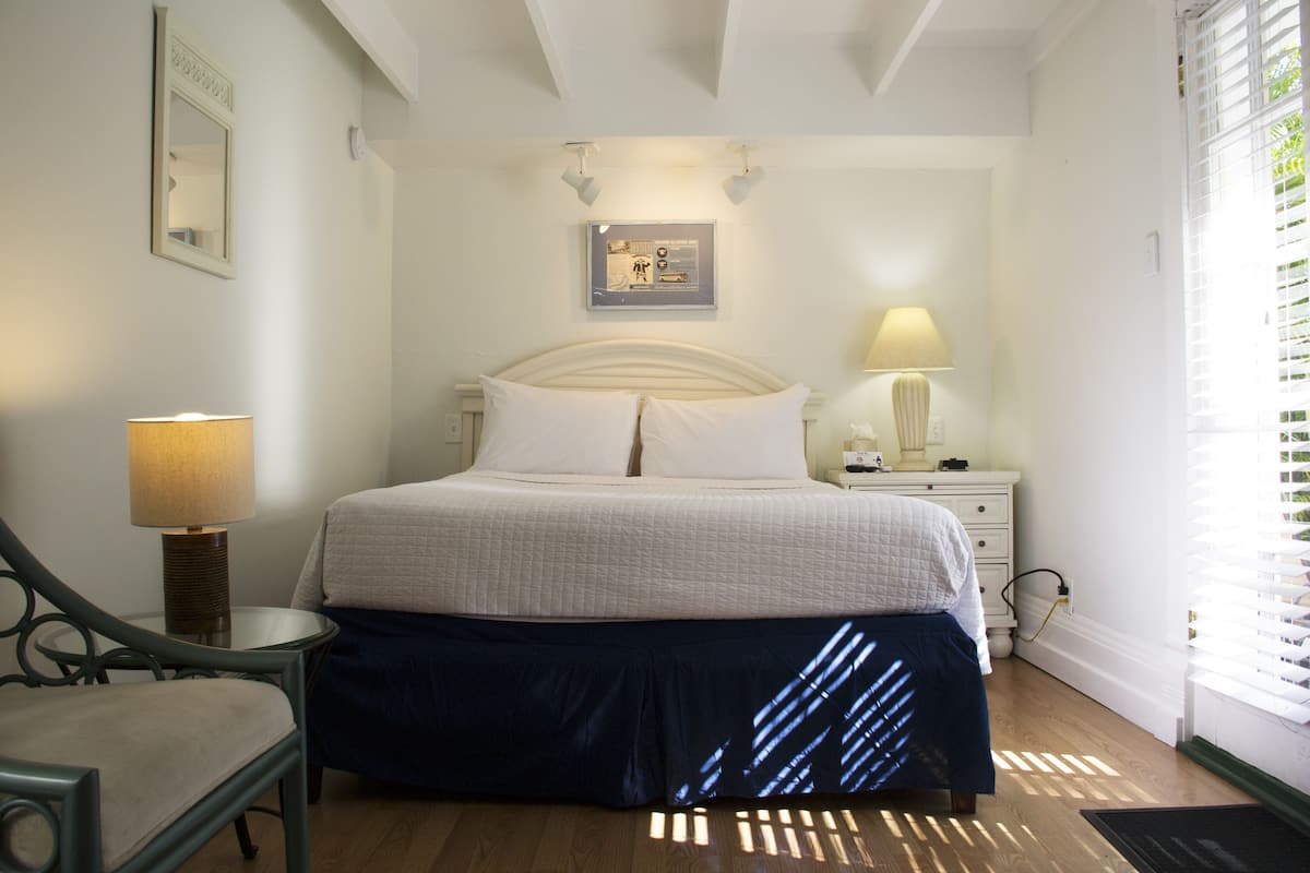 A bedroom with a bed, bedside tables, a chair, a lamp, and a framed picture on the wall.
