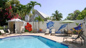 A swimming pool with a mural of a dolphin and a butterfly, surrounded by lounge chairs and palm trees. - Duval House (Key West)