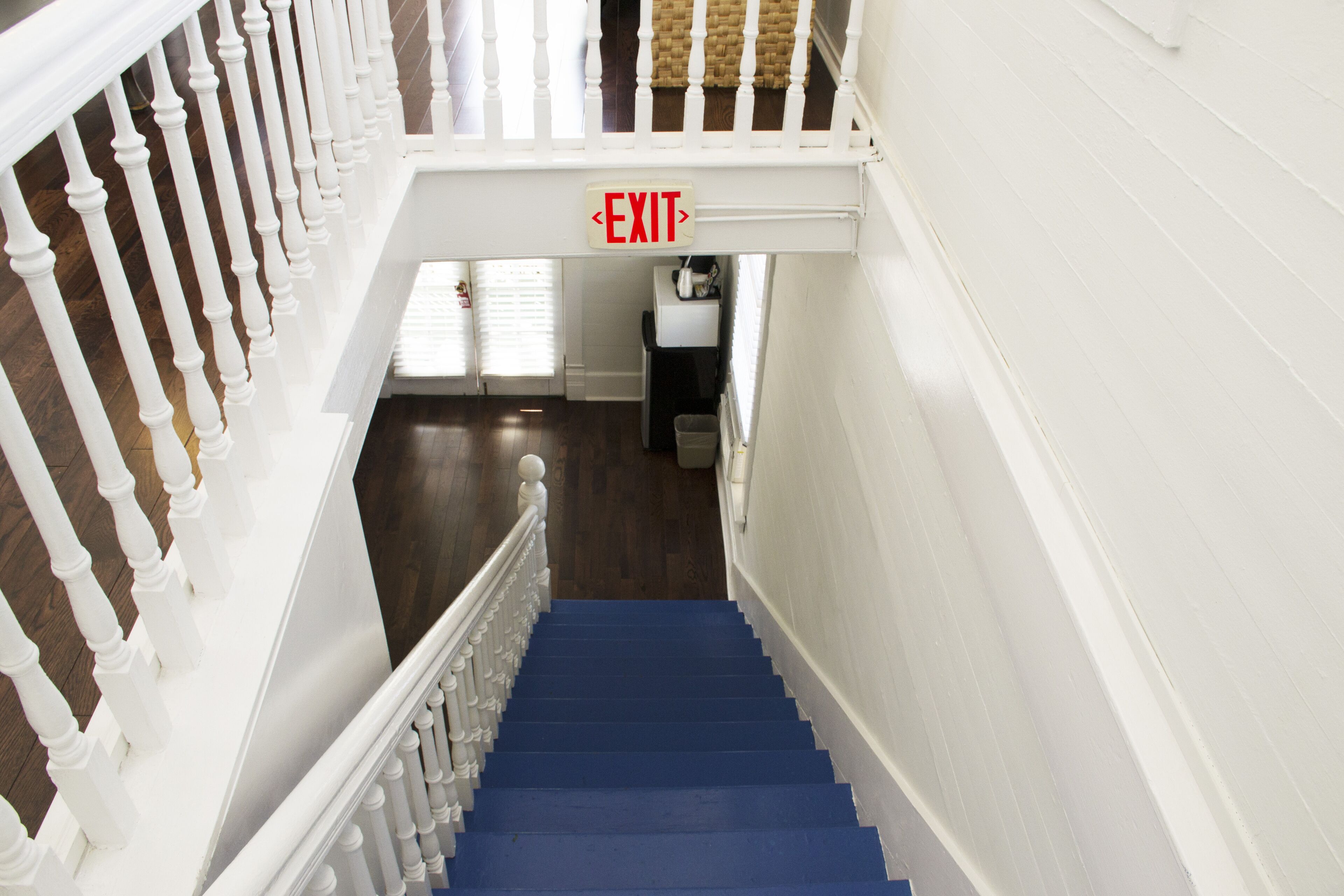 A staircase with white balusters and blue steps leading to an exit.