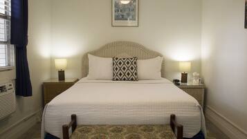 A neatly made bed with a headboard, two bedside lamps, a framed picture above the bed, and a bench at the foot of the bed.