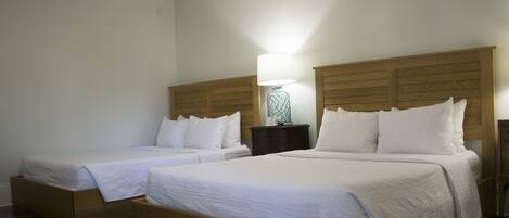 A hotel room with two single beds, wooden headboards, white bedding, a nightstand with a lamp, and a wooden floor.