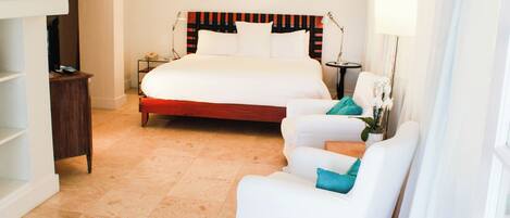 Een hotelkamer met een groot bed, een bureau, een stoel en een klein tafeltje met een lamp.