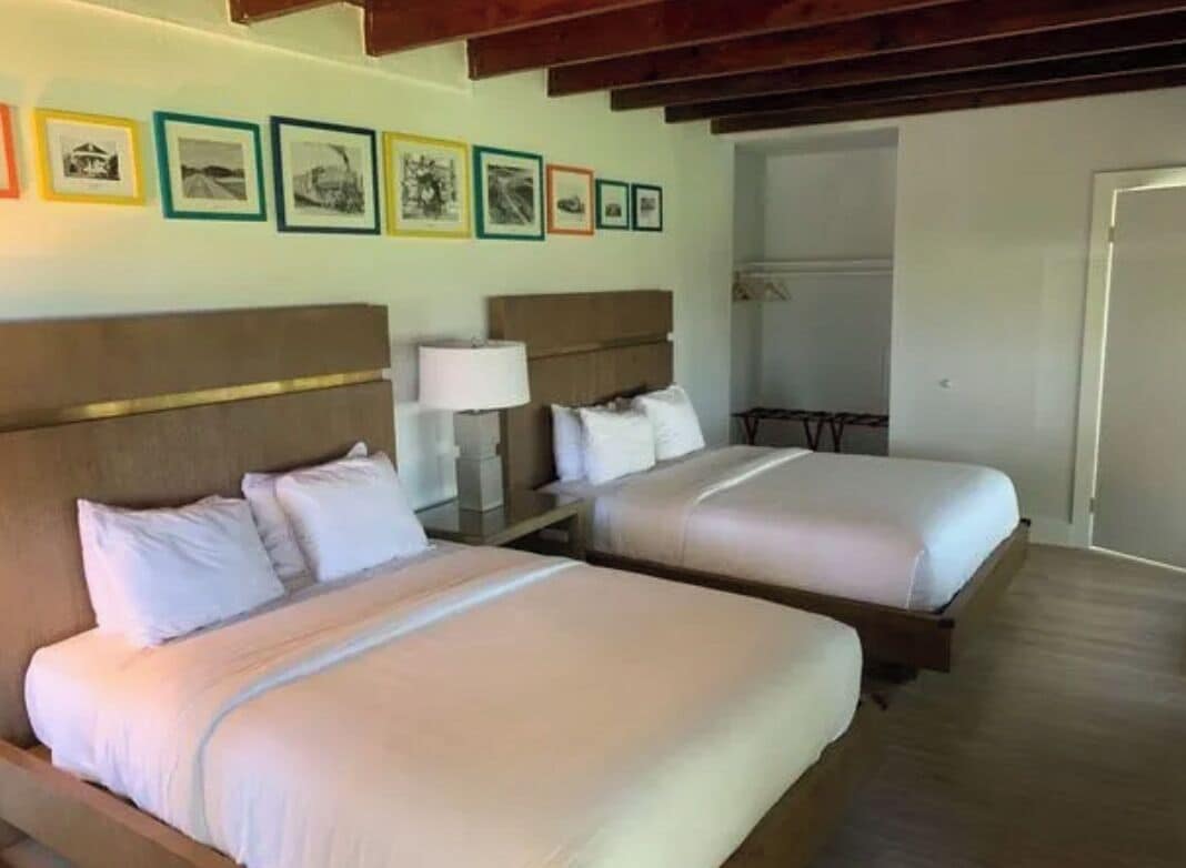 A hotel room with two beds, a wooden ceiling, and a wall with framed pictures.