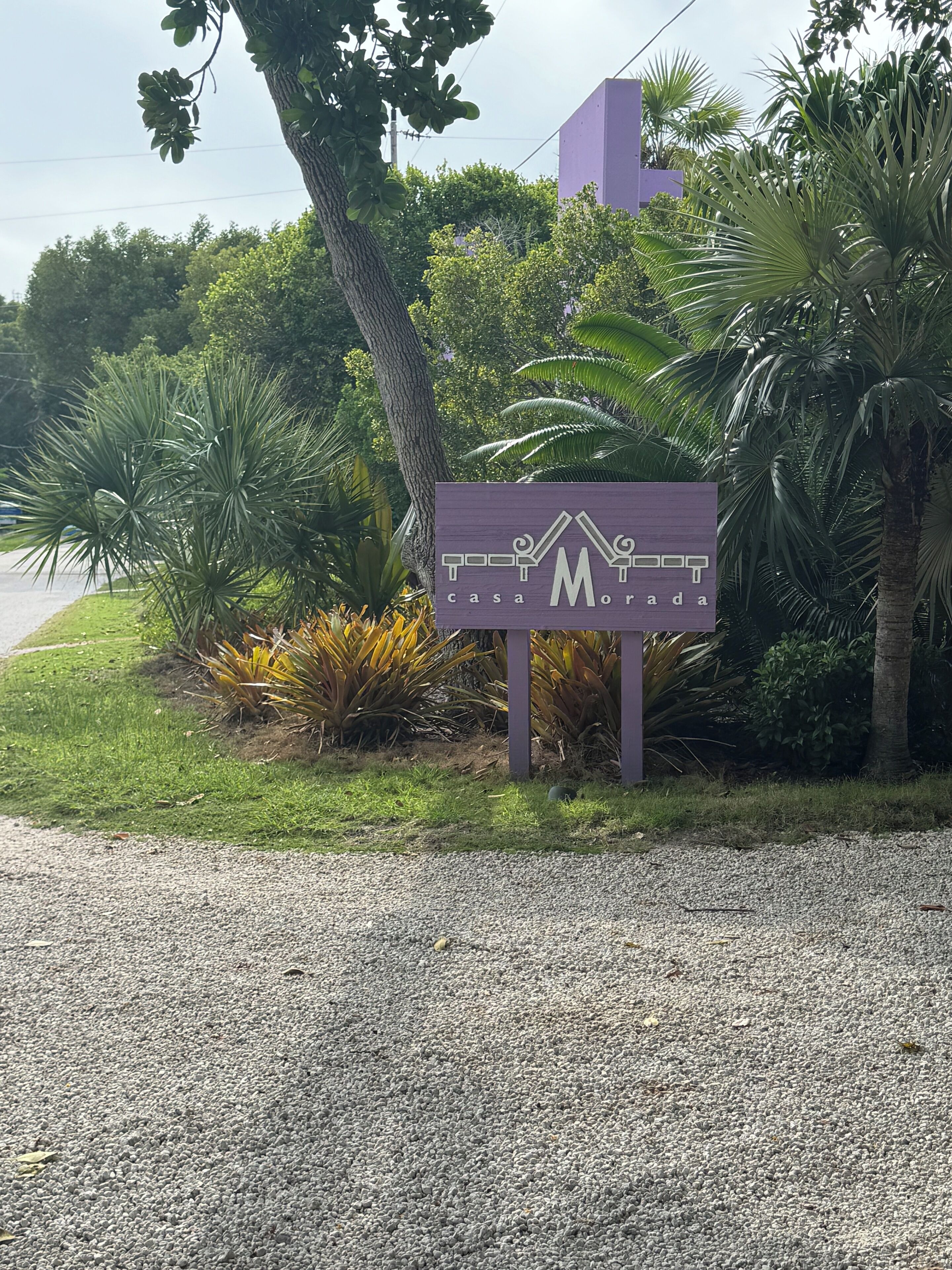 A sign for 'Casa Morada' with a modern design, surrounded by lush greenery and palm trees.