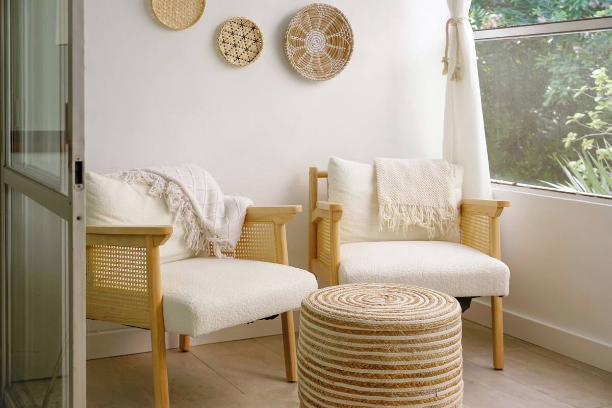 Quarto com duas cadeiras de vime, um banquinho tecido e três painéis decorativos.