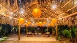 Une structure en bois à l’intérieur, dotée d’un toit de chaume, de plusieurs lampes sphériques suspendues et d’un espace salon central.