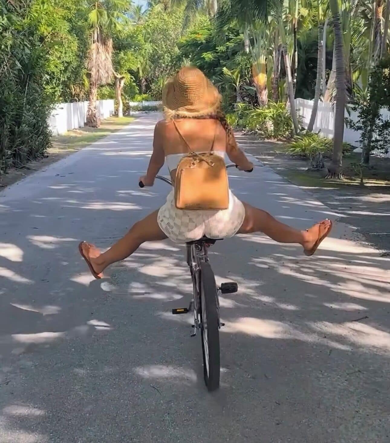 Eine Person vollführt eine Fahrradstunt auf einer asphaltierten Straße, umgeben von viel Grün.
