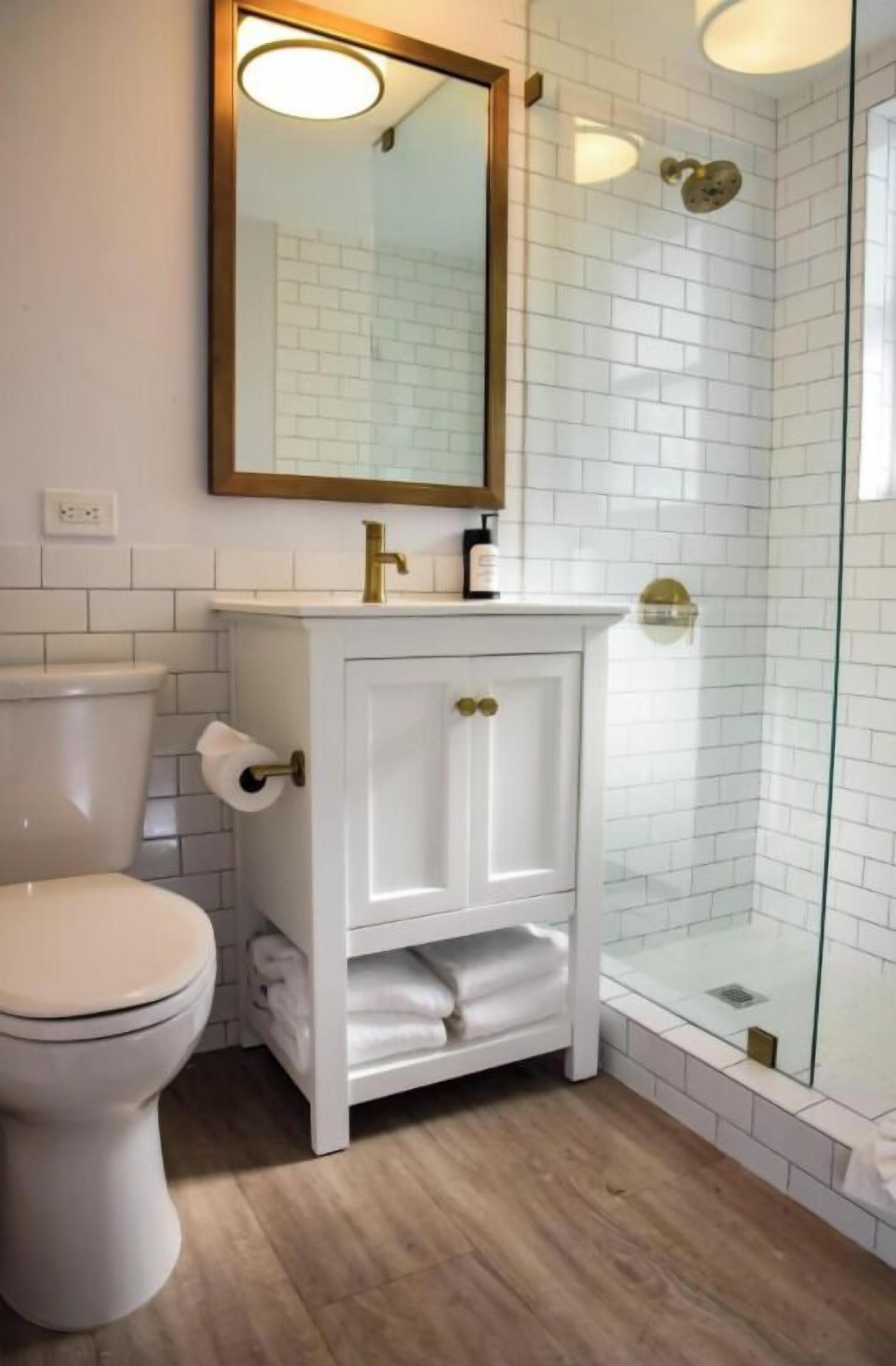 Ein Badezimmer mit Toilette, einem weißen Waschtisch mit goldenen Griffen, einem Spiegel und einer Duschkabine aus Glas.