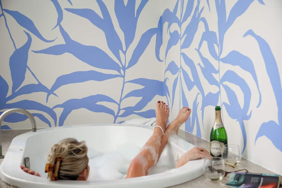 A person relaxing in a bathtub with a bottle of champagne and glasses on the side.