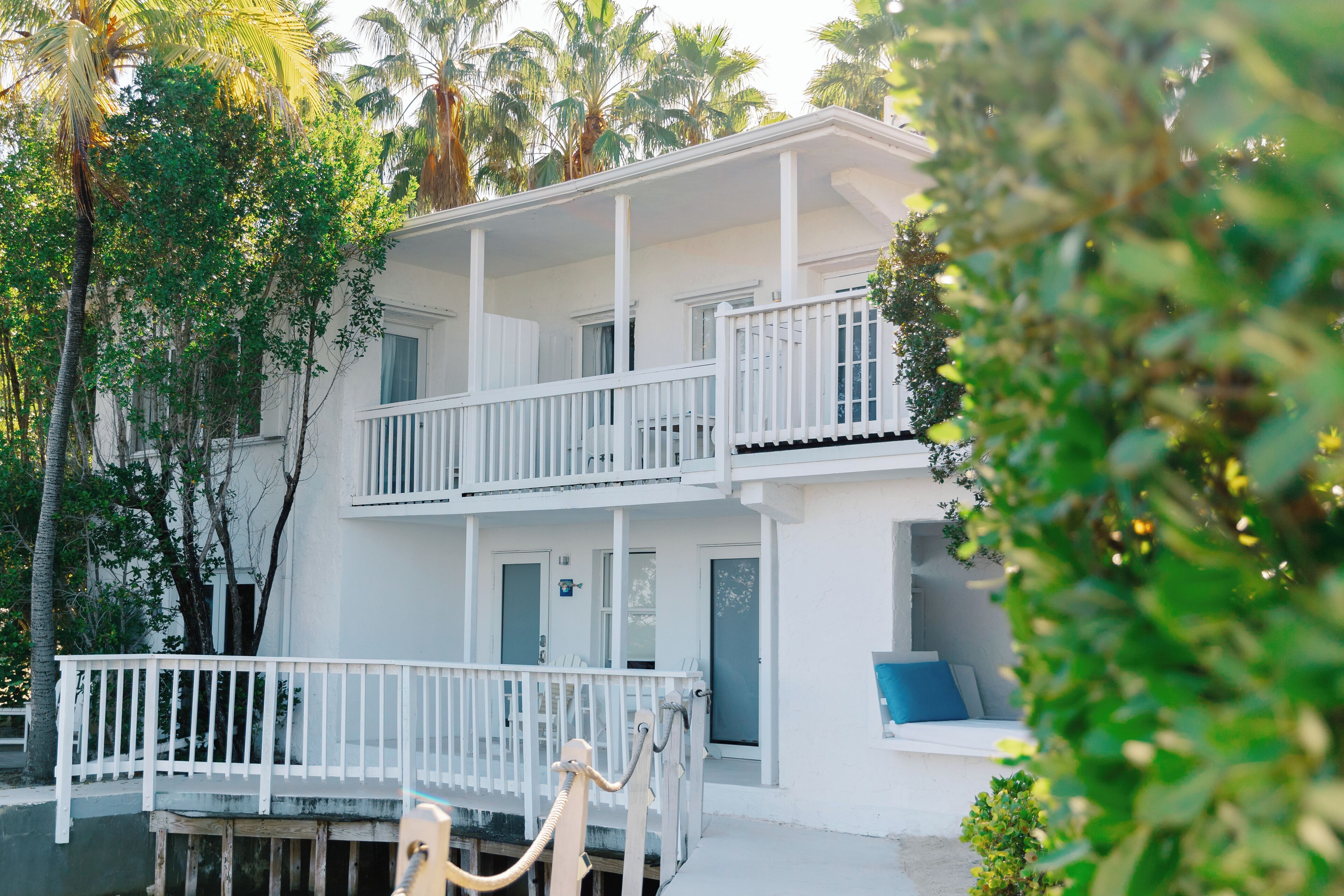 A two-story white building with balconies, surrounded by palm trees.