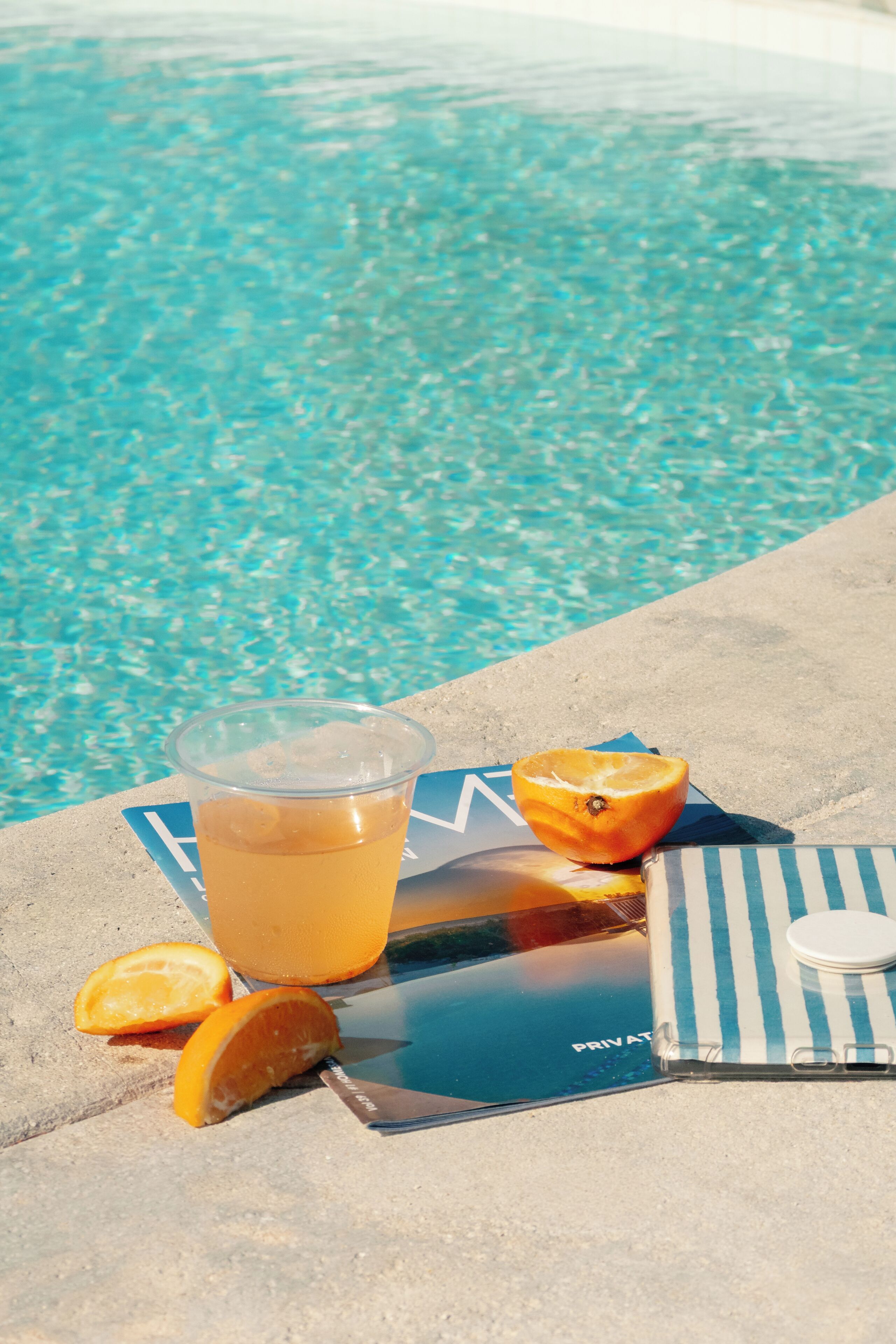 Vista clara de una piscina con una bebida y rodajas de naranja en el borde.