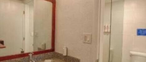 A bathroom with a granite countertop, a red-framed mirror, a white sink, a glass shower enclosure, and a white toilet.