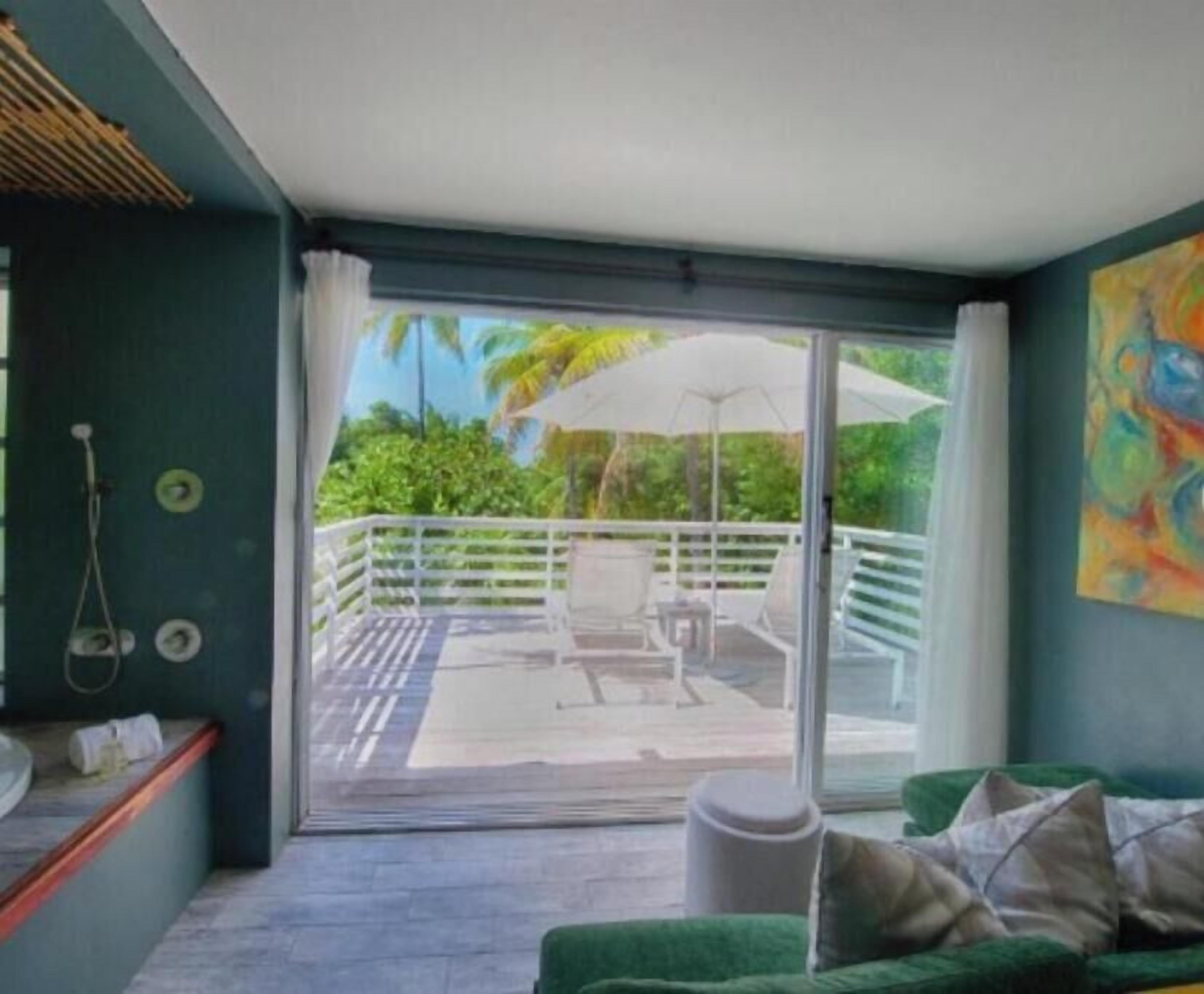 A room with a sliding glass door leading to an outdoor patio with a table and chairs, a green couch, and a painting on the wall.