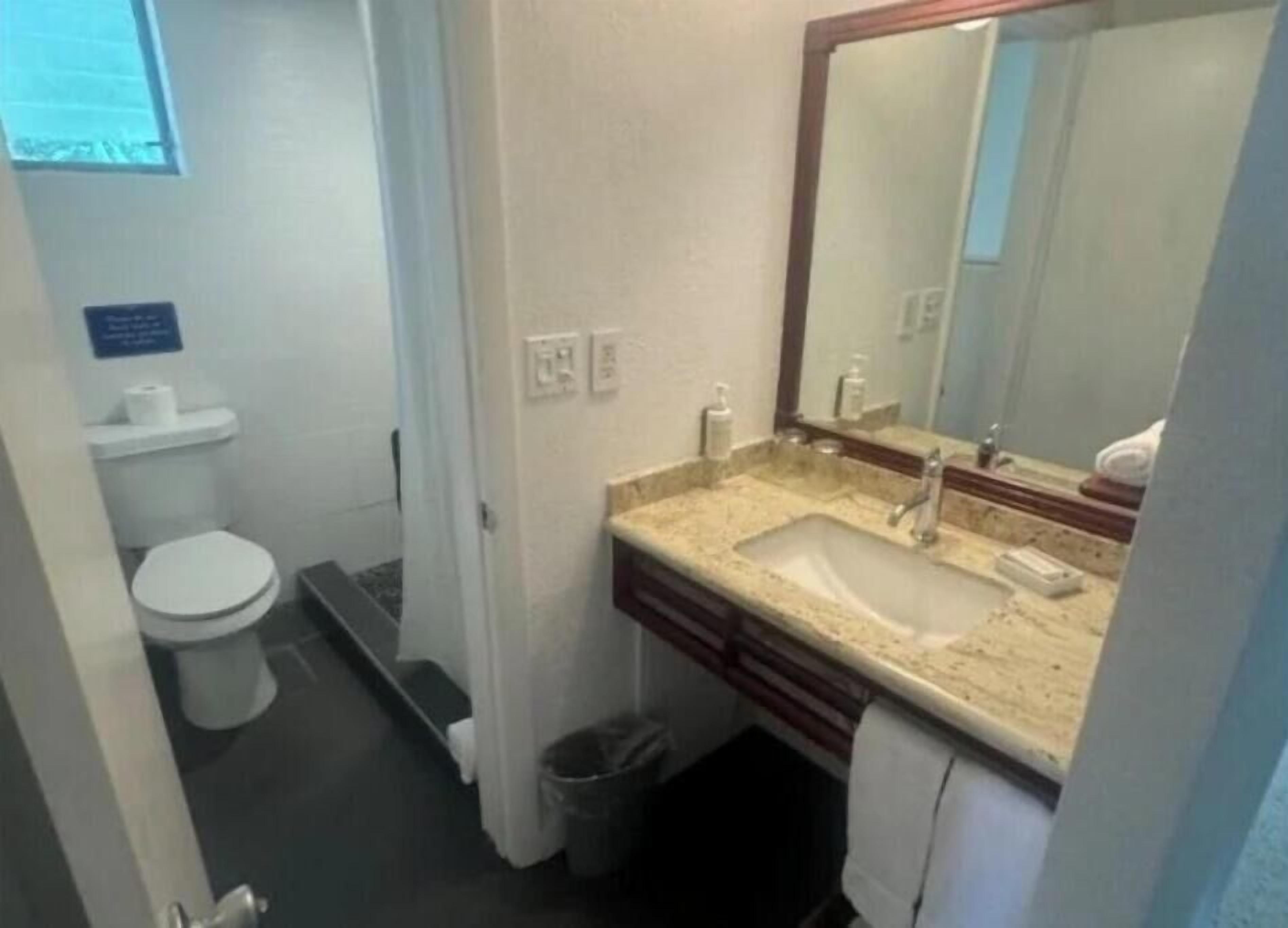 Ein kleines Badezimmer mit Toilette, Waschbecken, Spiegel und Mülleimer.
