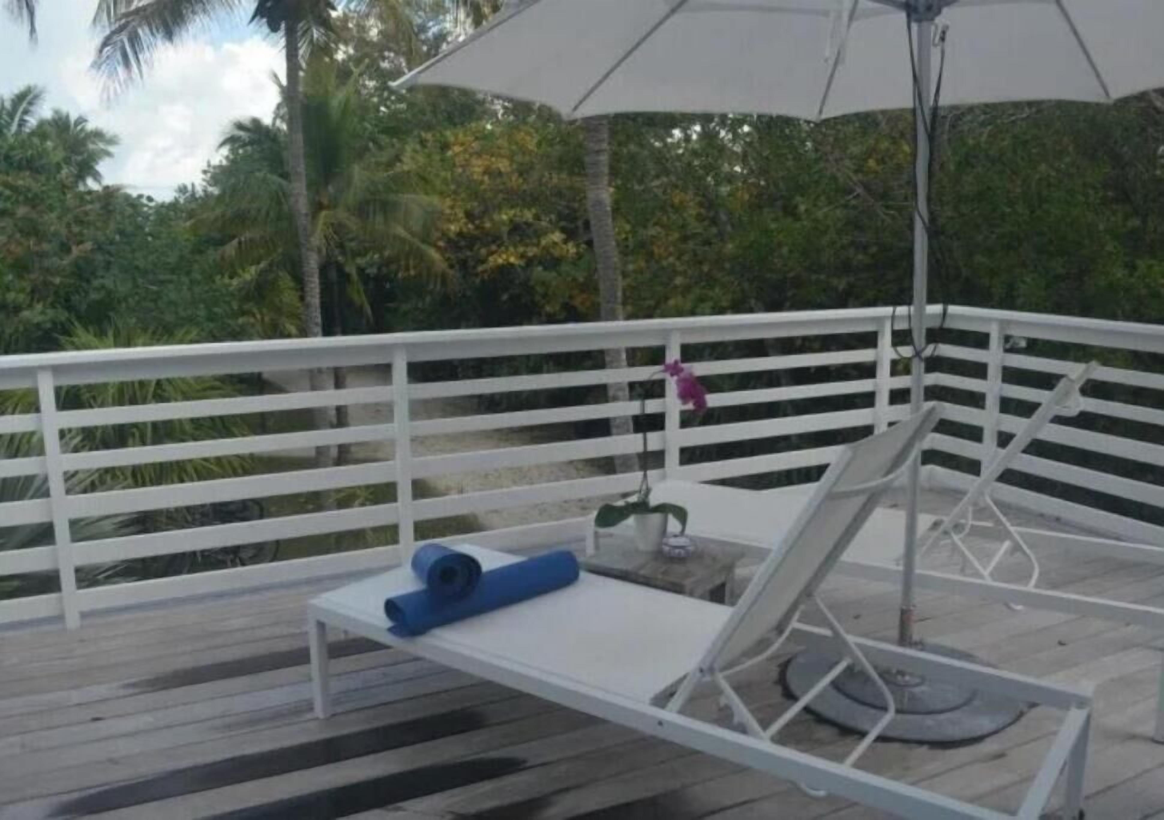 Une terrasse dotée d’une rambarde blanche, d’une chaise longue, d’une serviette bleue et d’un grand parasol.