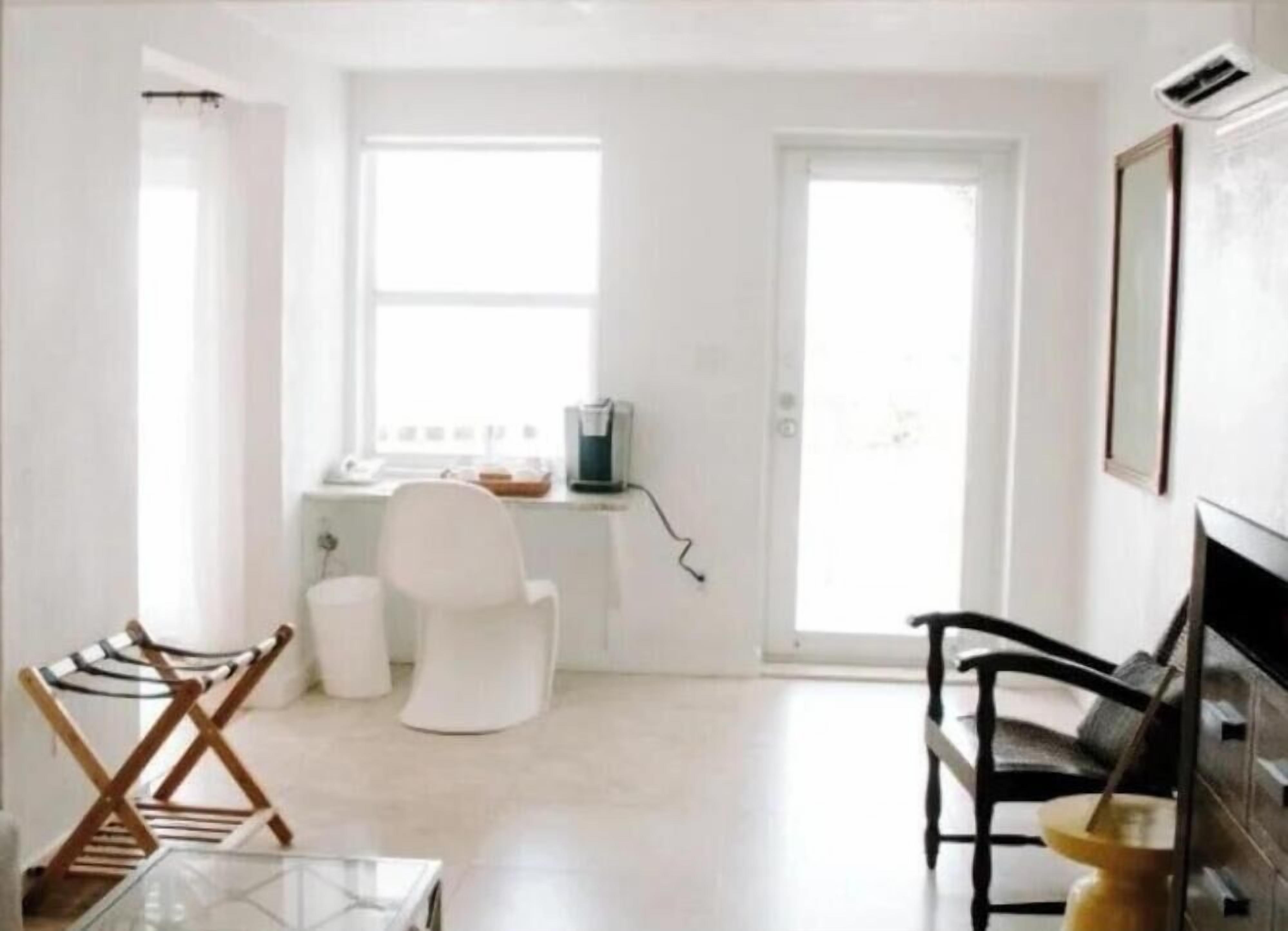Ett kompakt bostadsutrymme med ett litet kök, en vit stol, en svart soffa och ett glasbord.