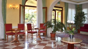 A lobby with checkered flooring, red upholstered chairs, a round wooden table, and potted plants. - Hotel Villa Cipro (Venice)