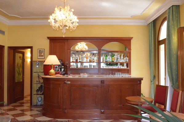 Una zona de bar con mostrador de madera, estantes con botellas y una araña.