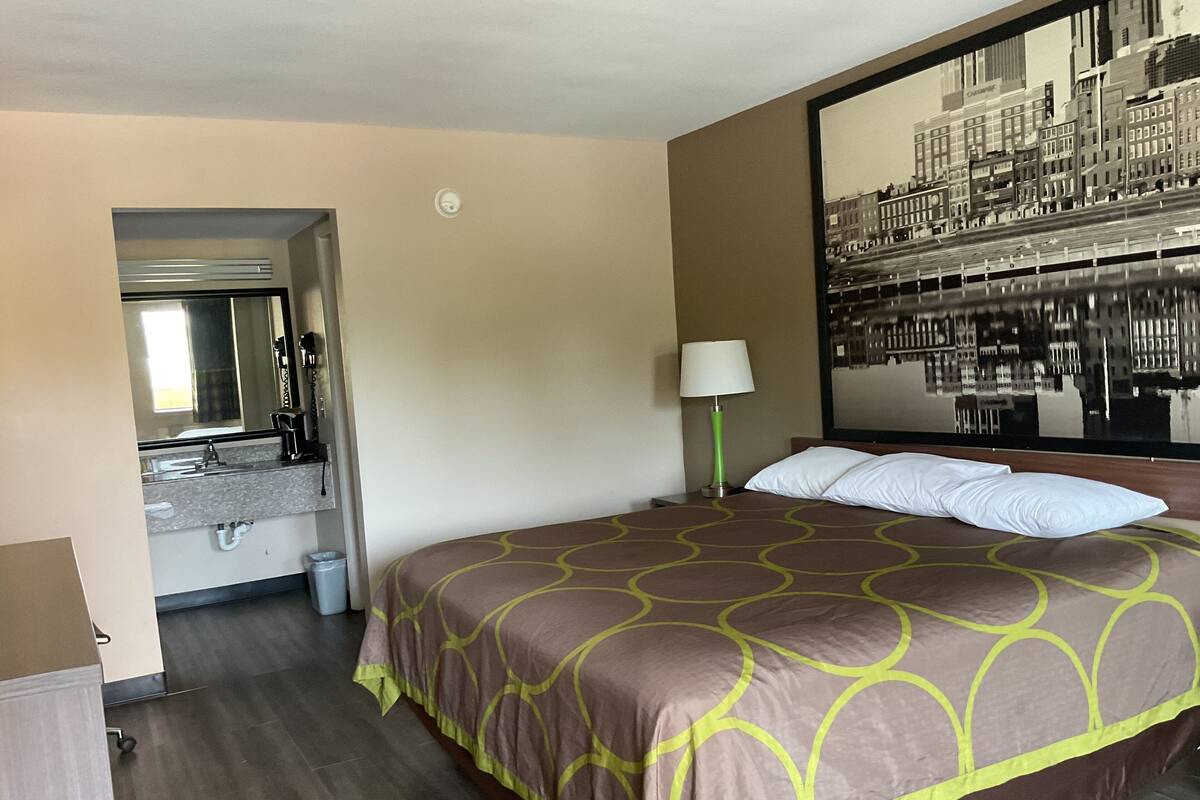A hotel room with a bed, a bathroom with a sink and mirror, and a large cityscape mural on the wall.
