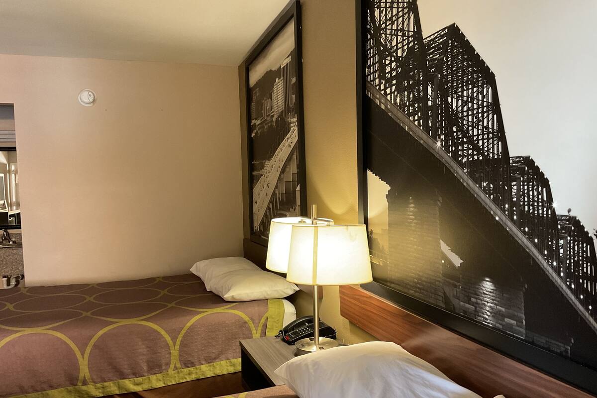 A hotel room with two beds, a nightstand, a lamp, a telephone, and a large framed picture of a bridge.