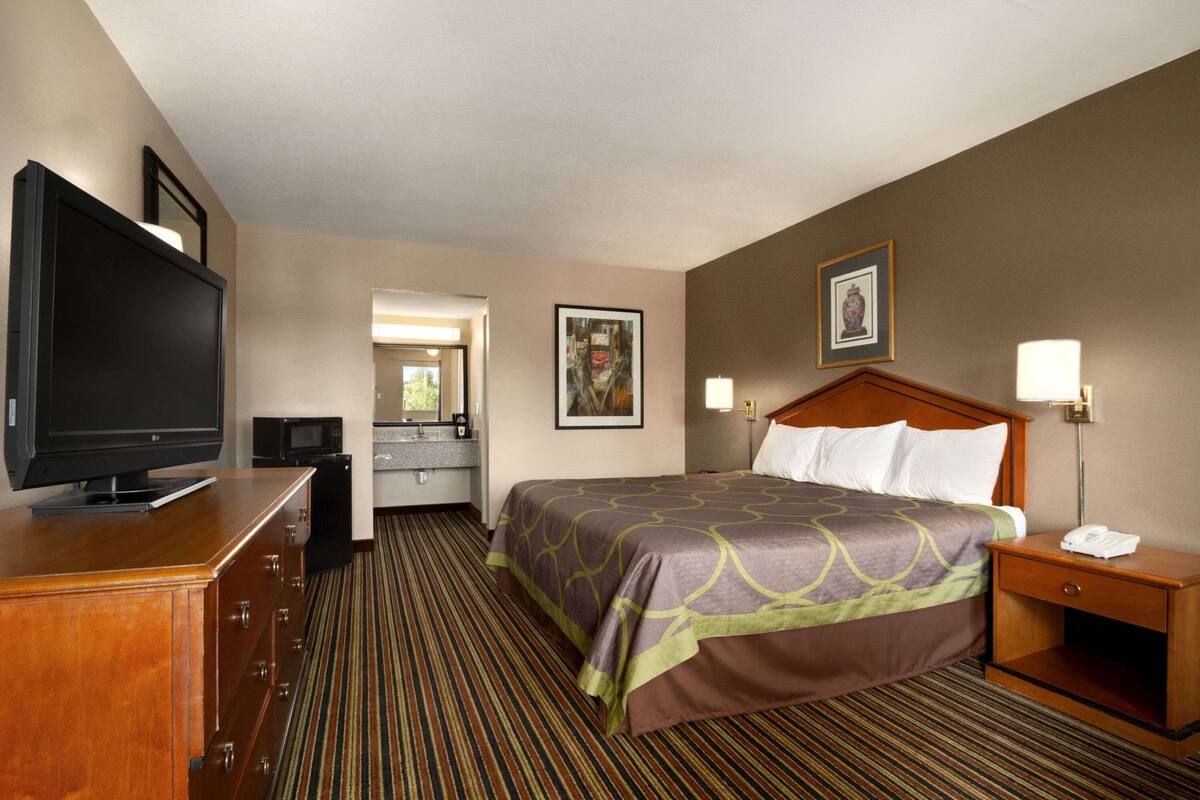 A hotel room with a bed, a television, a desk, a nightstand, and a bathroom.