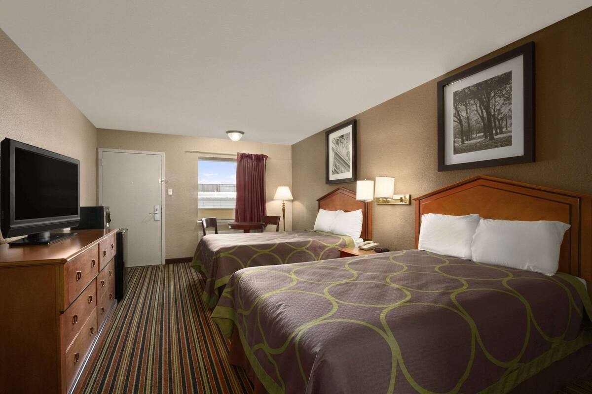 A hotel room with two beds, a television, a desk, and a window with curtains.