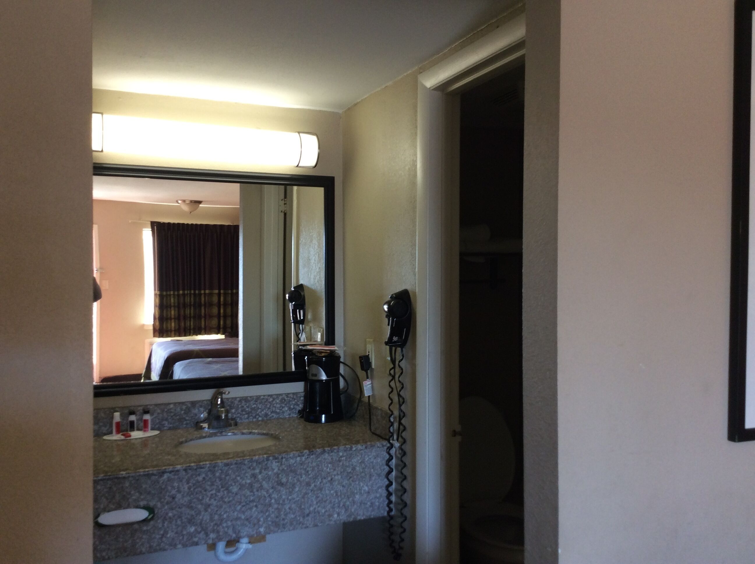 A hotel bathroom with a sink, mirror, hairdryer, and a coffee maker.